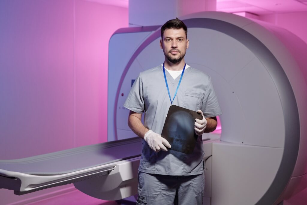 MRI technologist standing in from of an MRI machine holding X-ray results.