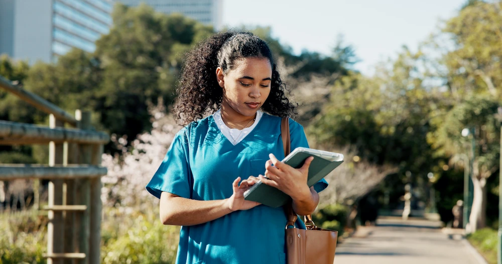 Travel nurse reviewing her expenses on an iPad while walking in a park.