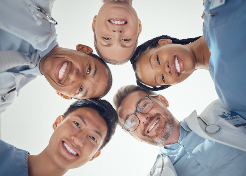 Smiling medical team standing in a circle and looking down at the camera.
